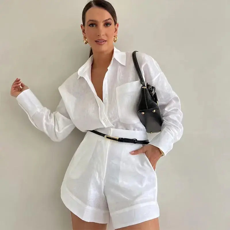 Woman wearing a white outfit with a black handbag against a plain background