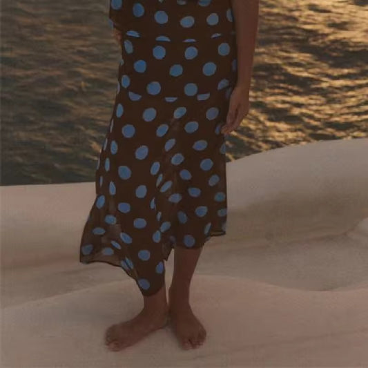 Person wearing a brown dress with blue polka dots by the water at sunset.