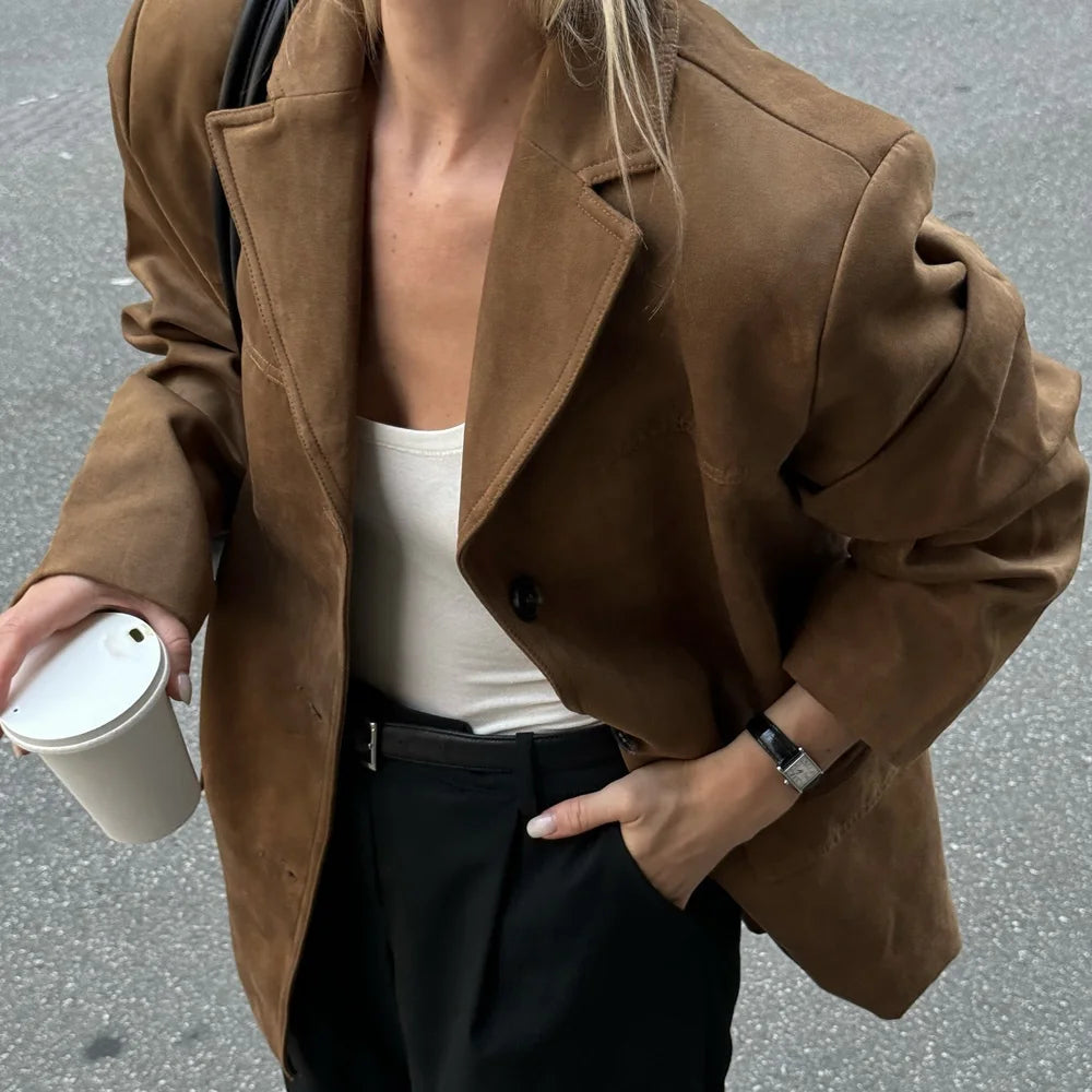 Person wearing a brown coat holding a coffee cup on a street.