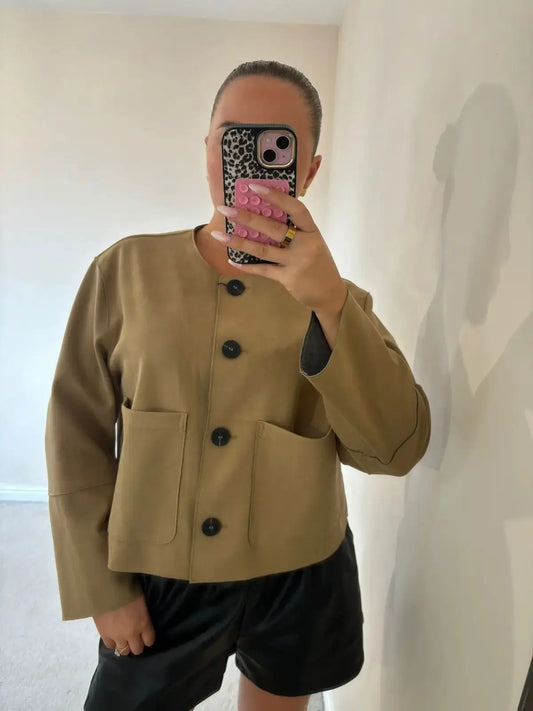 Person wearing a beige jacket with black buttons in a minimal indoor setting.