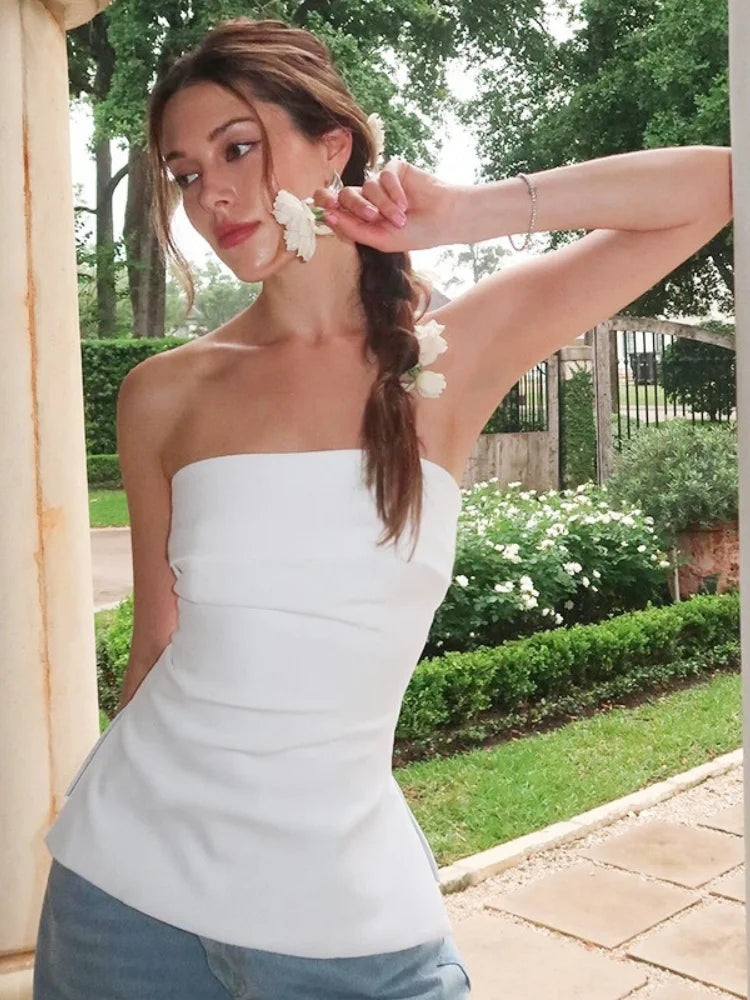 Woman wearing a strapless white top outdoors with greenery in the background