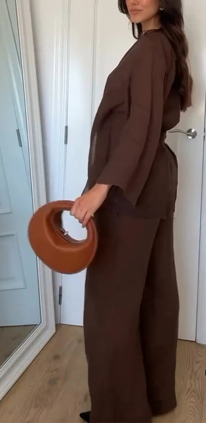 Person wearing a brown outfit holding a brown bag in a room with white walls and wooden floor.