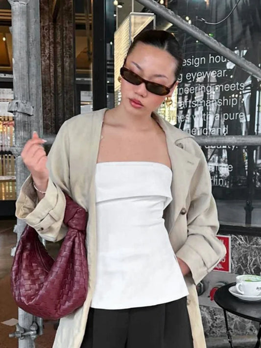 Person wearing a beige coat, white strapless tube top, and dark sunglasses indoors.